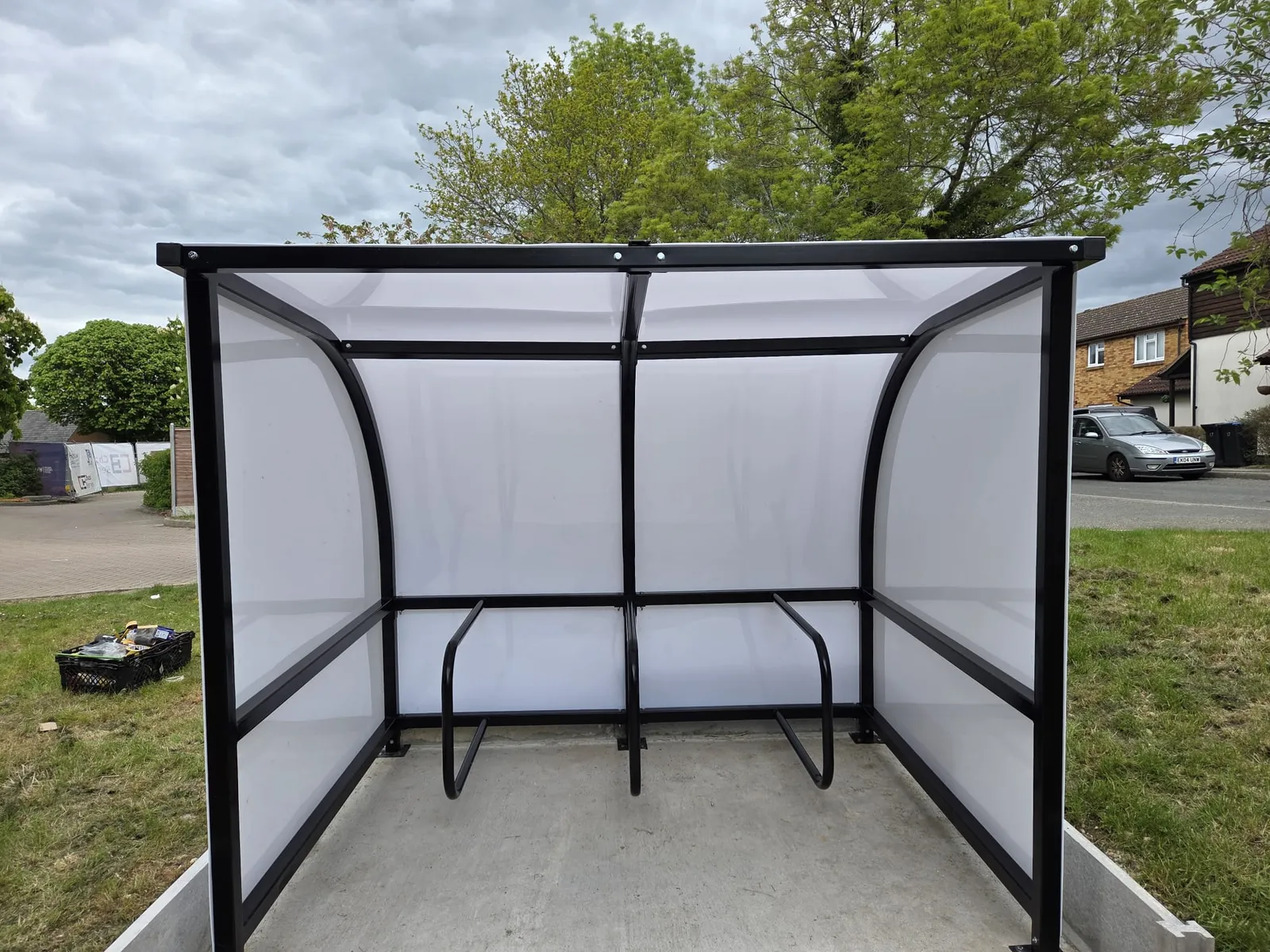 Steel cycle shelter with frosted polycarbonate side panels and cycle hoops on a residential street
