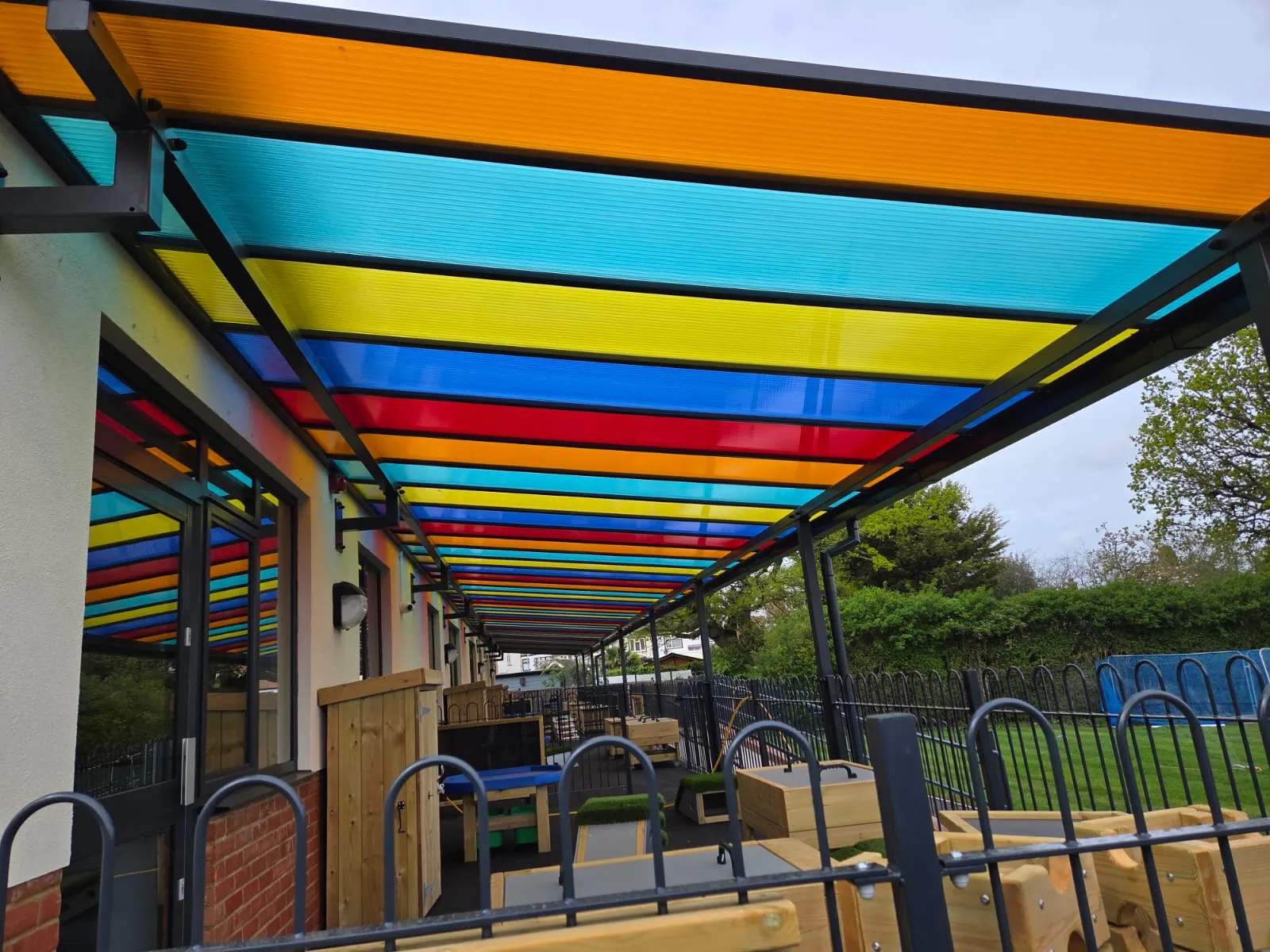 Multi-coloured polycarbonate covered walkway canopy running the length of a school building